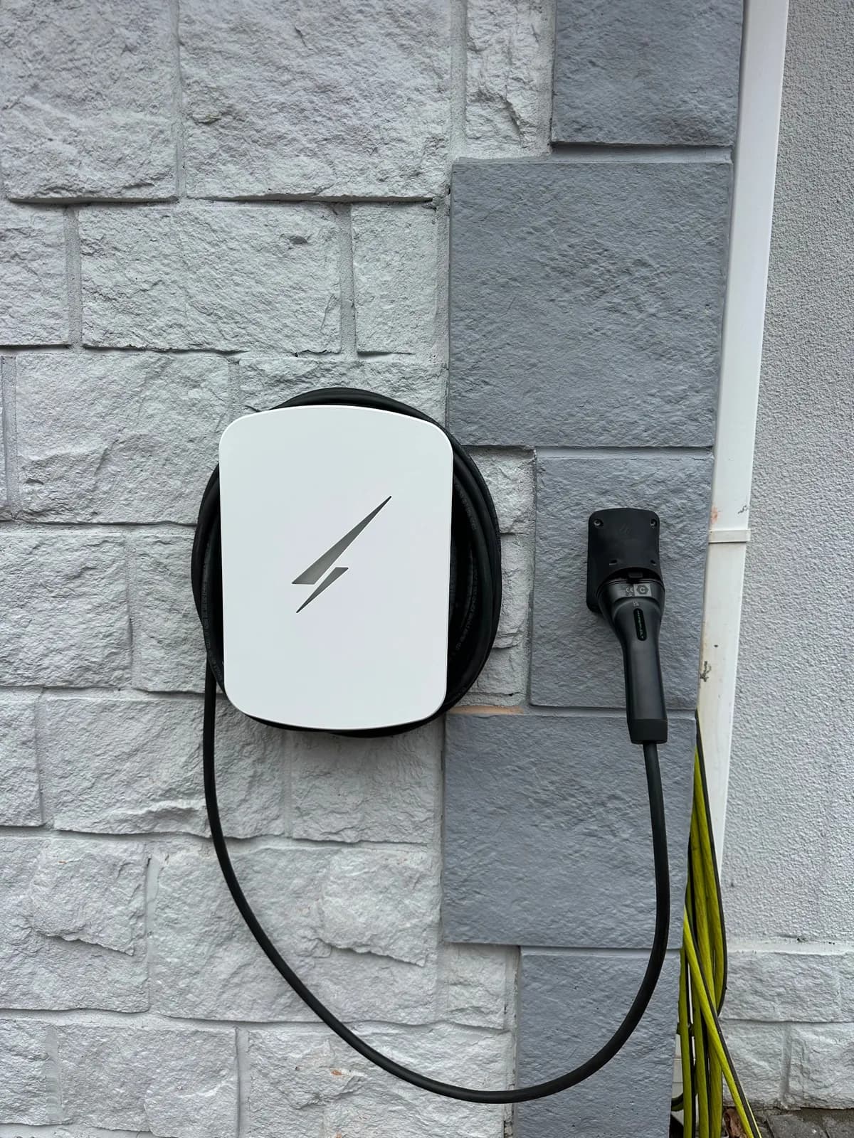 White tethered EV charger fitted to a painted stone-effect wall, holster to the right